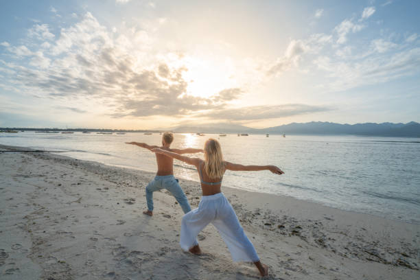 Healthy young couple exercising yoga outdoors on the beach at sunrise in a tropical climate, Bali, Indonesia. People healthy balance concept
