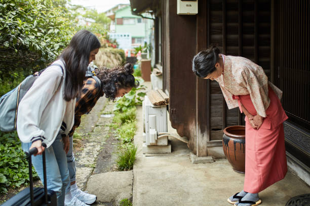 Mature landlady greeting young female guests at ryokan. Women are bowing in front of inn owner. They are standing outside hotel.